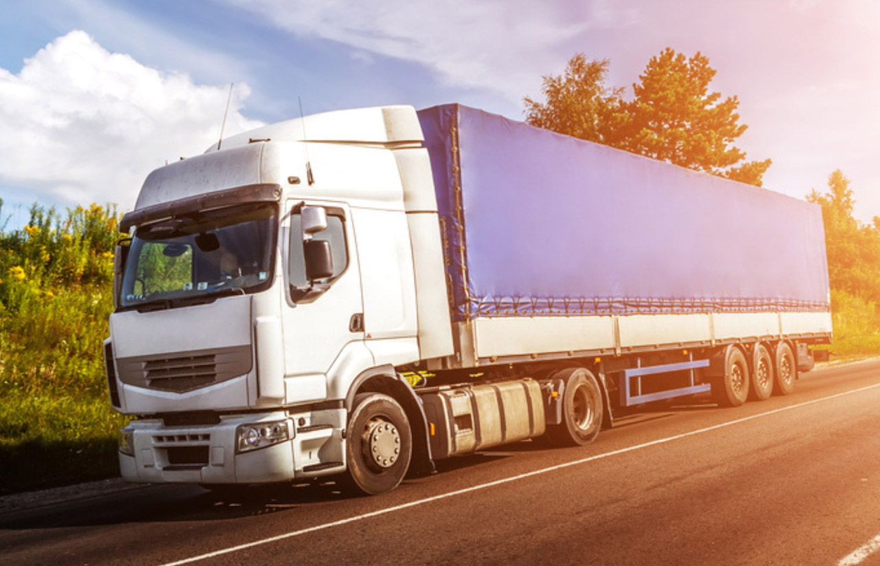 White semi-truck with a blue curtain-side trailer driving on a rural road at sunset